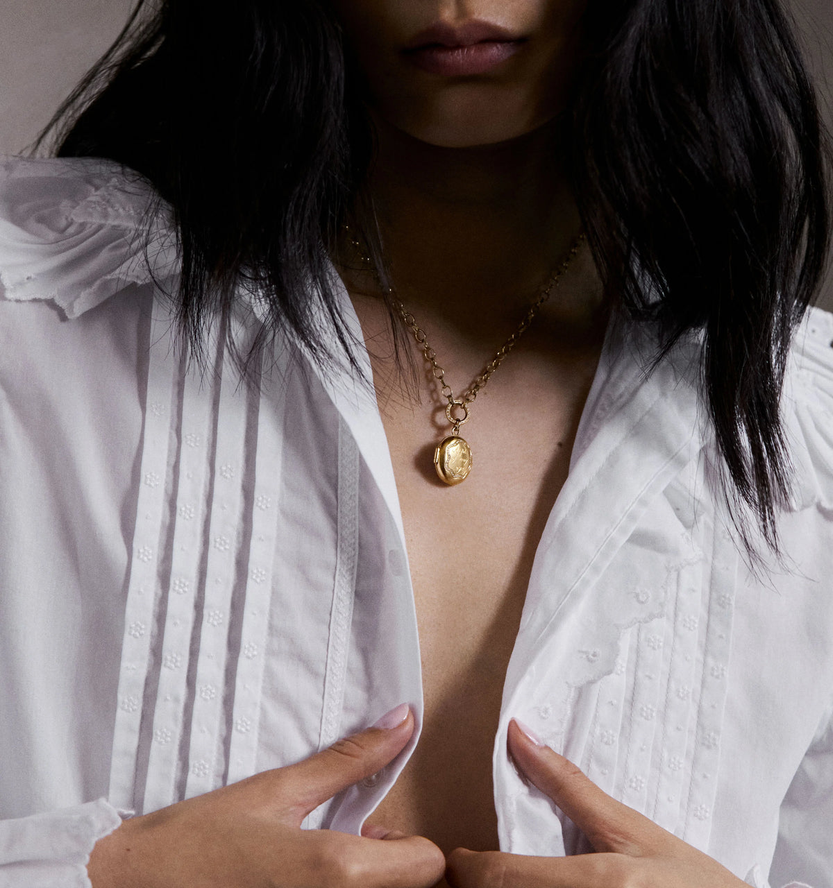Woman wearing a gold pendant necklace with an engraved design, paired with a white button-up shirt.