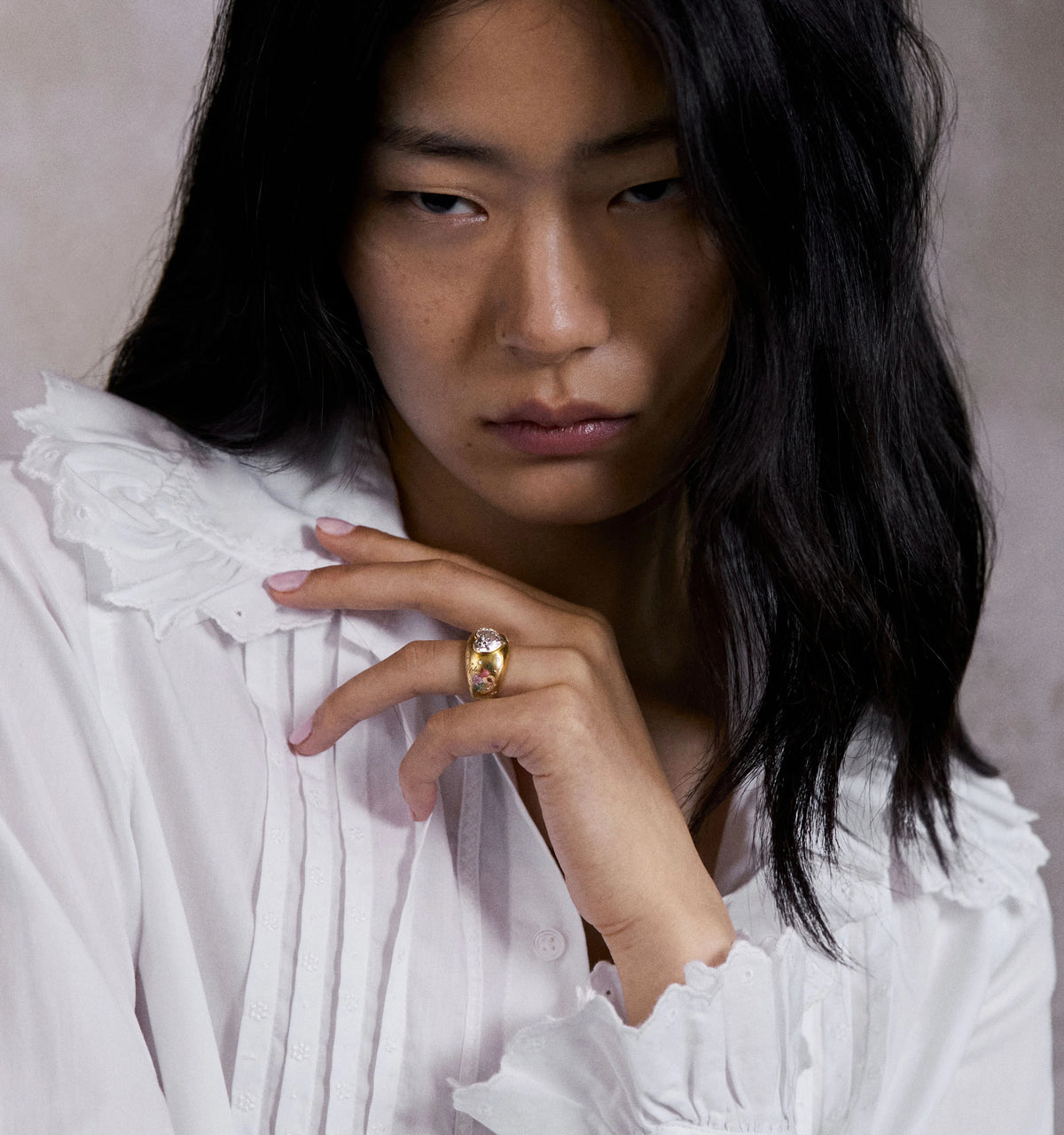Woman wearing a gold ring with a clear stone, dressed in a white blouse with ruffled collar.