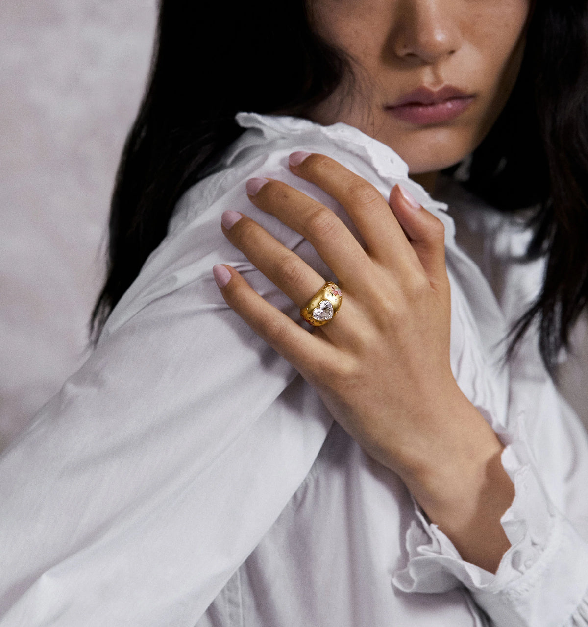 Woman wearing a gold ring featuring two heart-shaped diamonds, resting her hand on her shoulder.
