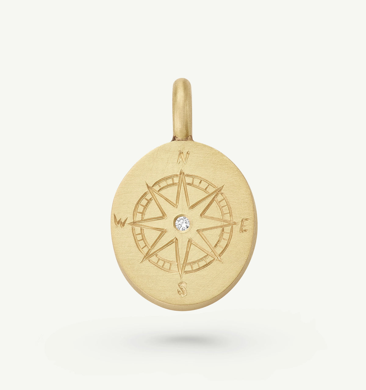 Gold compass pendant featuring an engraved design and a single diamond in the centre.