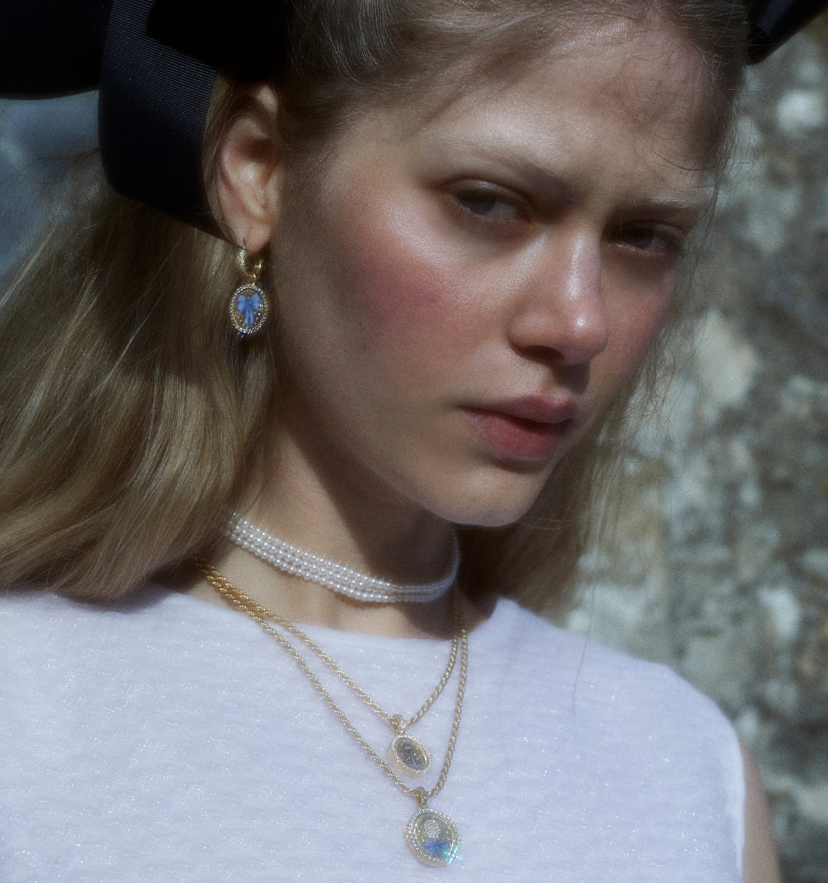 Woman wearing a gold necklace with a blue stone, gold earrings, and a layered pearl choker.