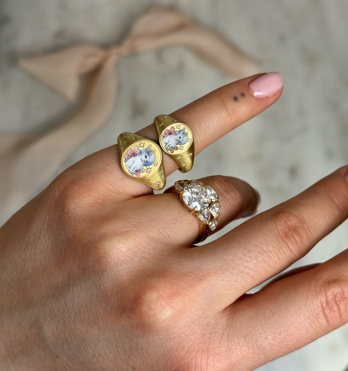 Woman wearing gold rings featuring bunny motifs and a gold ring set with a large oval clear stone.