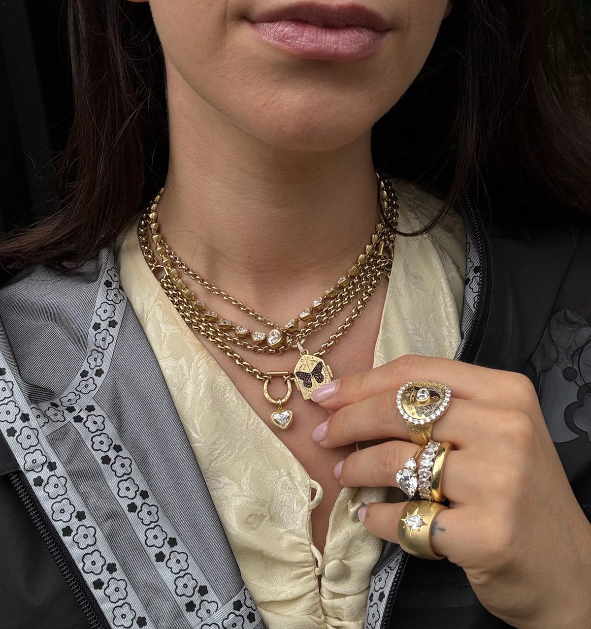 Woman wearing multiple gold chains, including a gold pendant and heart charm, with gold rings on her hand.