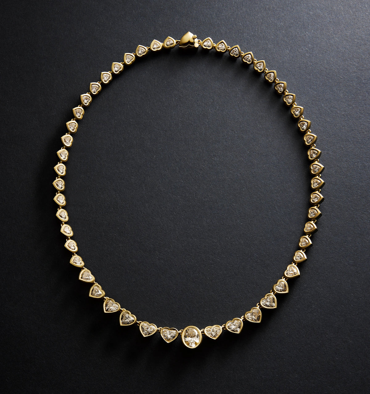 Gold necklace featuring heart-shaped links set with diamonds against a dark background.