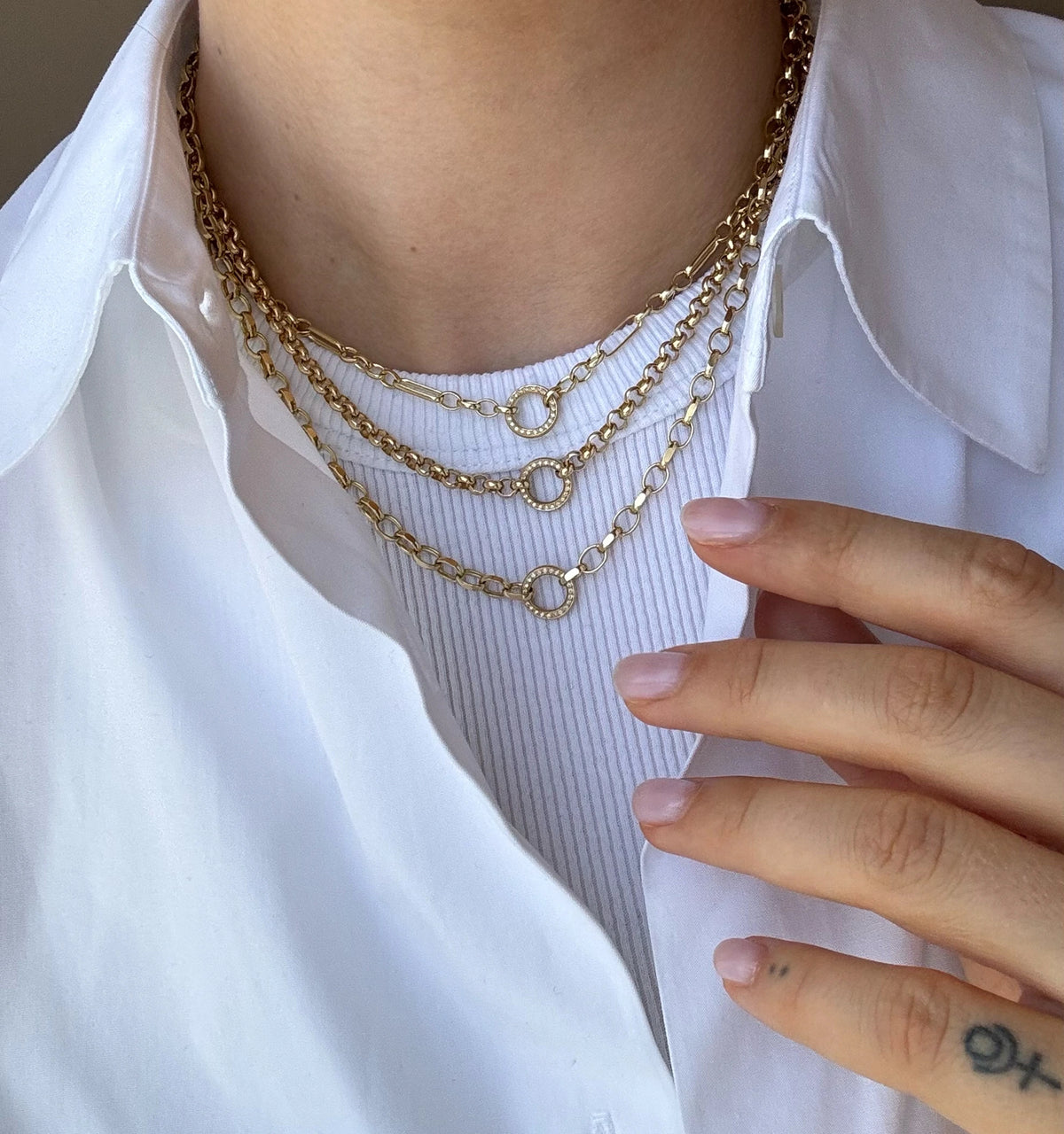 Woman wearing layered gold chain necklaces against a white shirt.