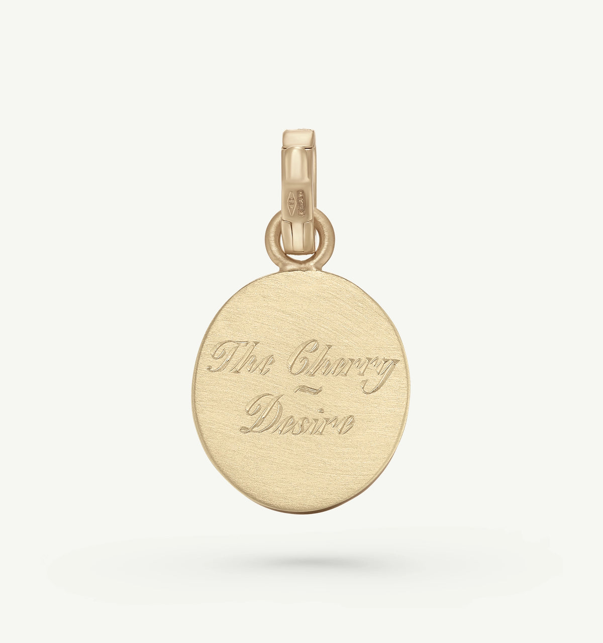 Gold pendant with engraved text reading "The Cherry of Desire" on a textured surface.