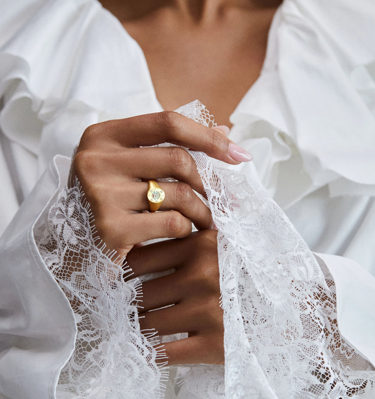 Woman wearing a gold ring with a floral design, holding delicate lace fabric.