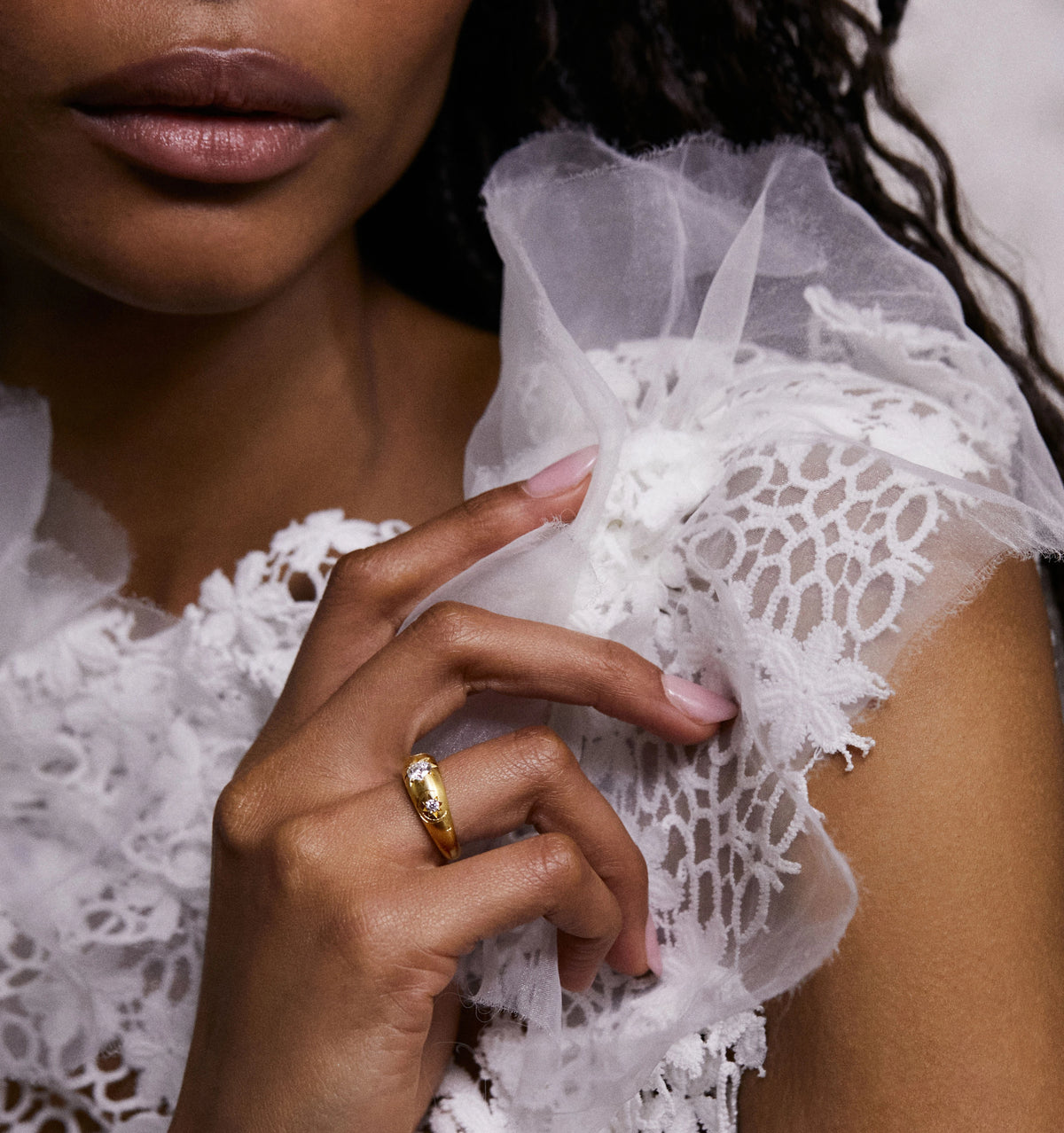Woman wearing a gold ring with a clear stone, delicately touching a lace and tulle garment.