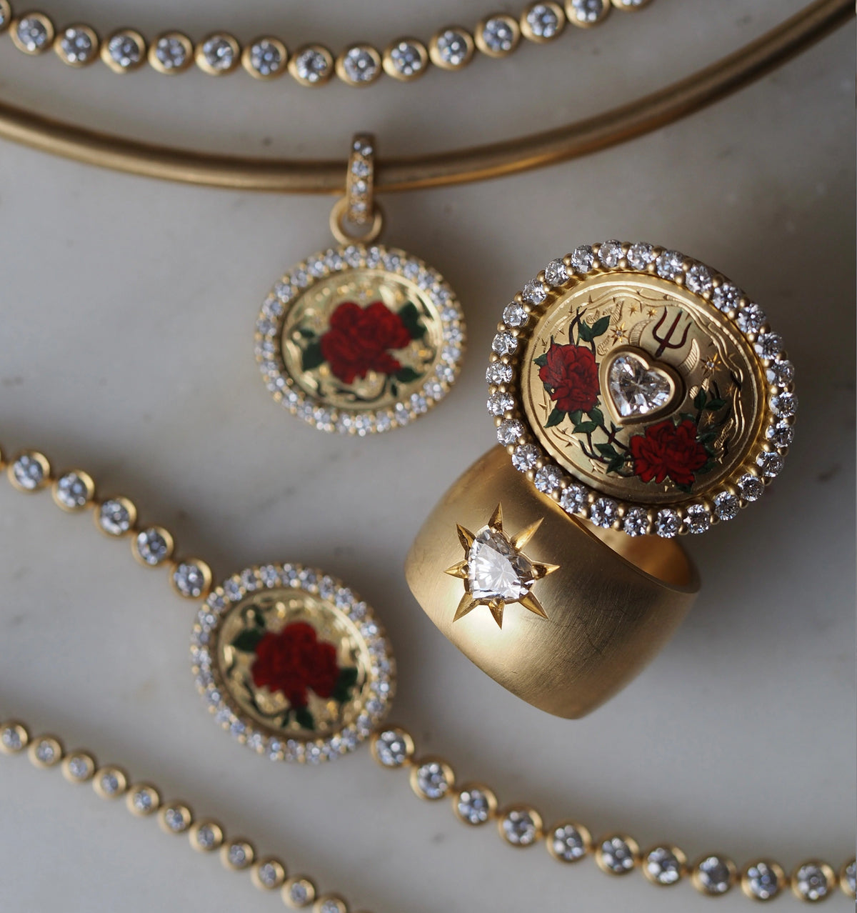 Gold necklace and earrings with red rose motifs and gold ring featuring a star-shaped diamond on a marble surface.