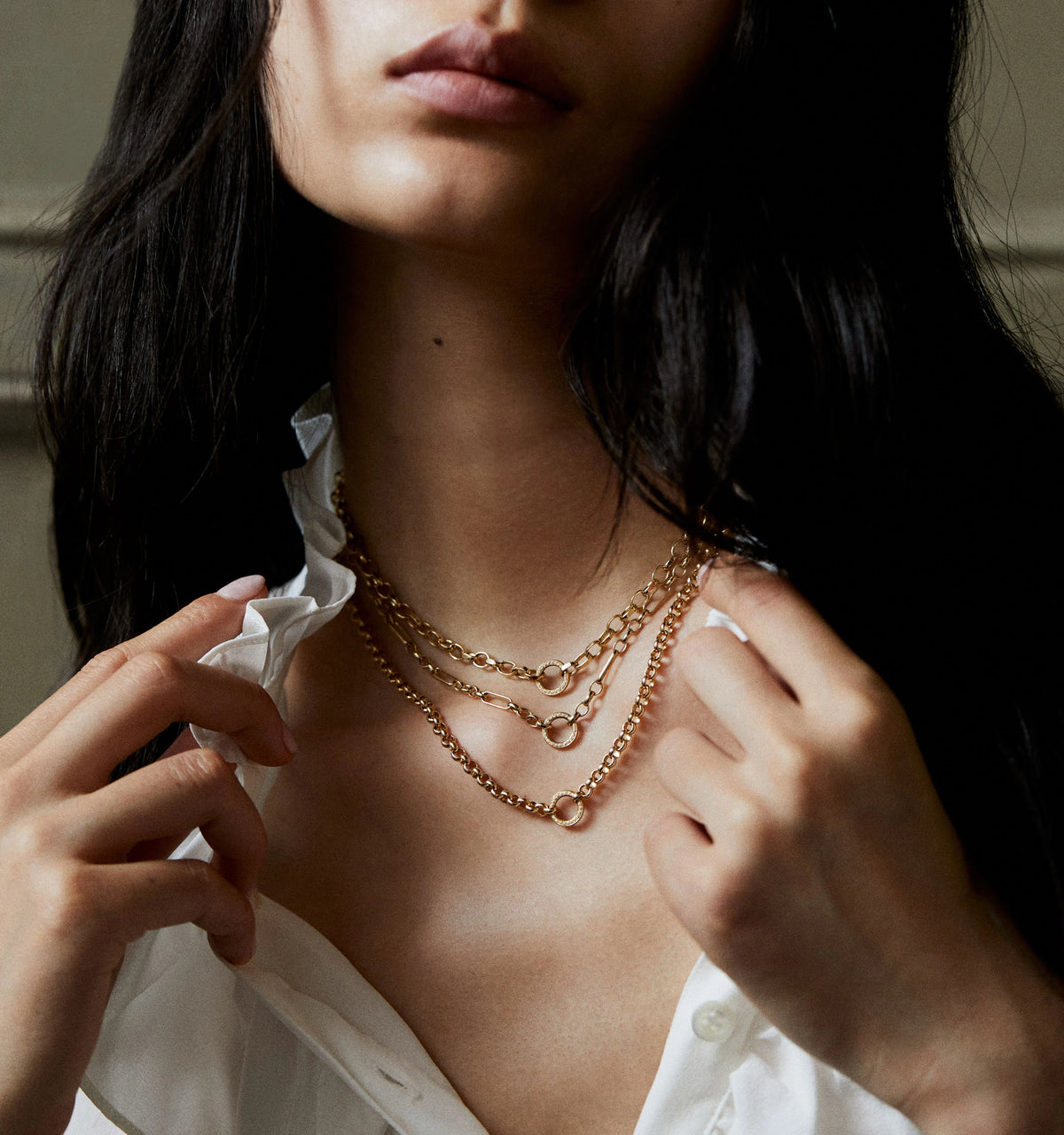 Woman wearing layered gold chain necklaces styled with a white blouse.