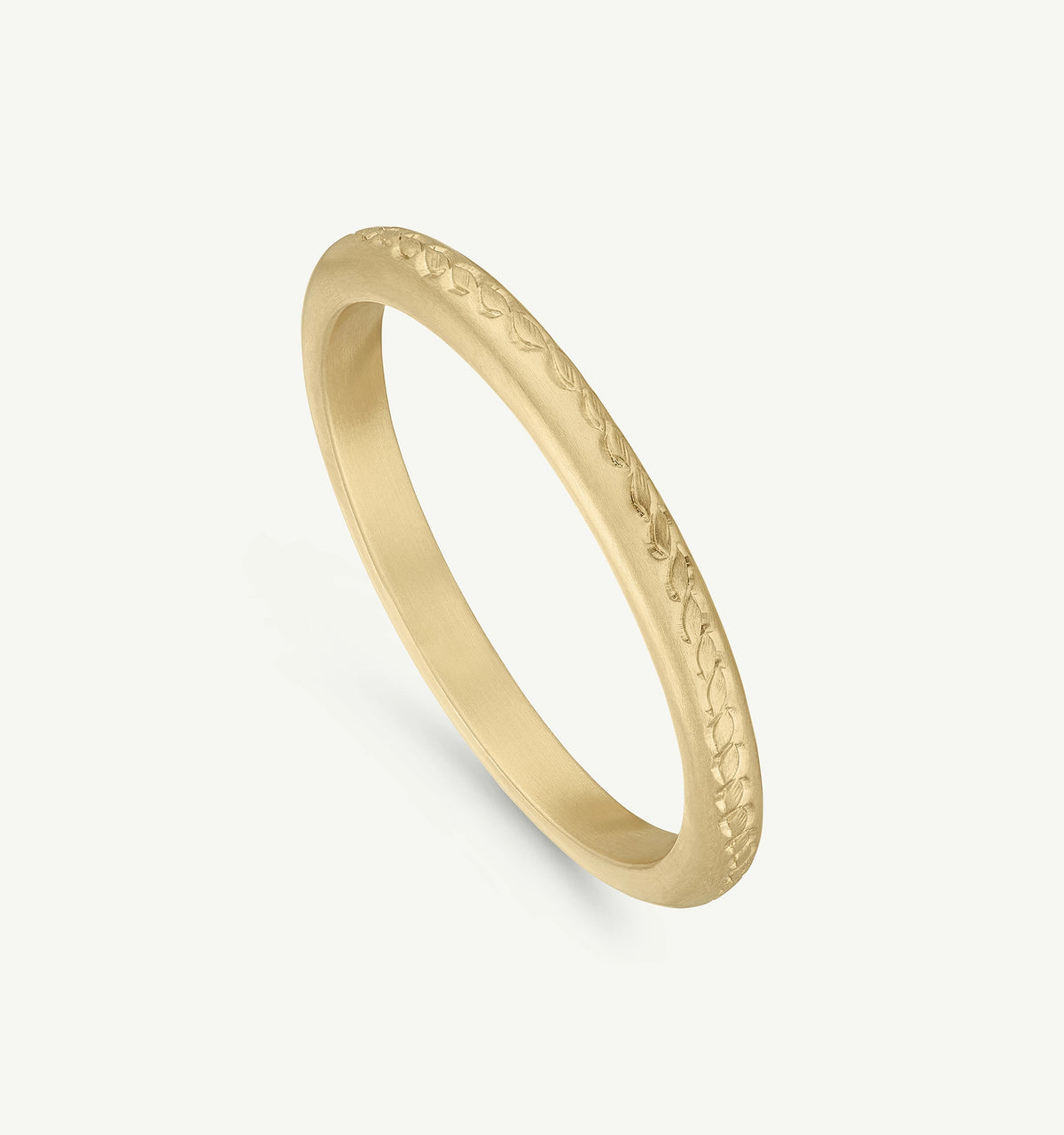 Gold ring with an engraved leaf pattern on a smooth surface.