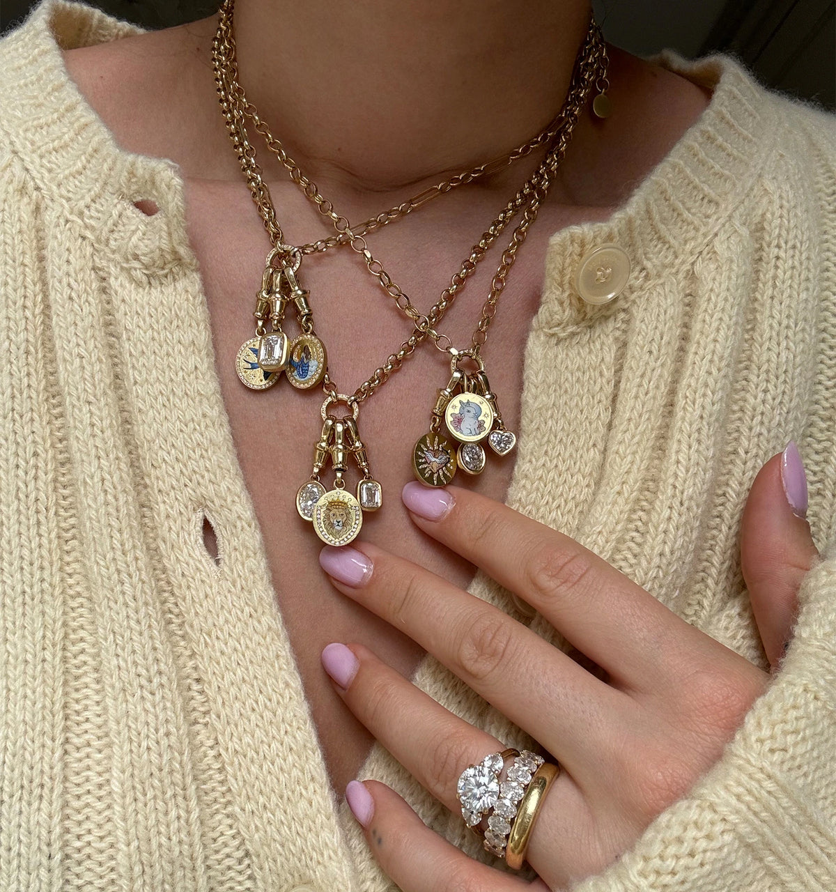 Woman wearing layered gold necklaces with lion, bird, and bunny enamel charms and diamonds, and gold rings with diamonds.