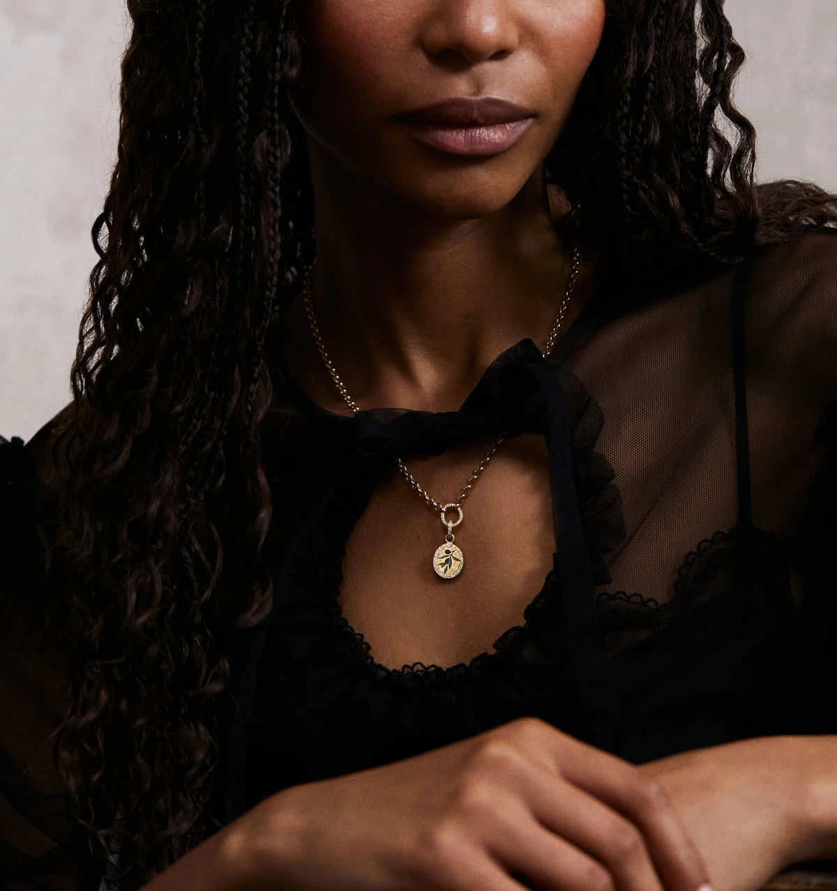 Woman wearing a gold pendant necklace featuring an engraved leaf design, styled with a black sheer blouse.
