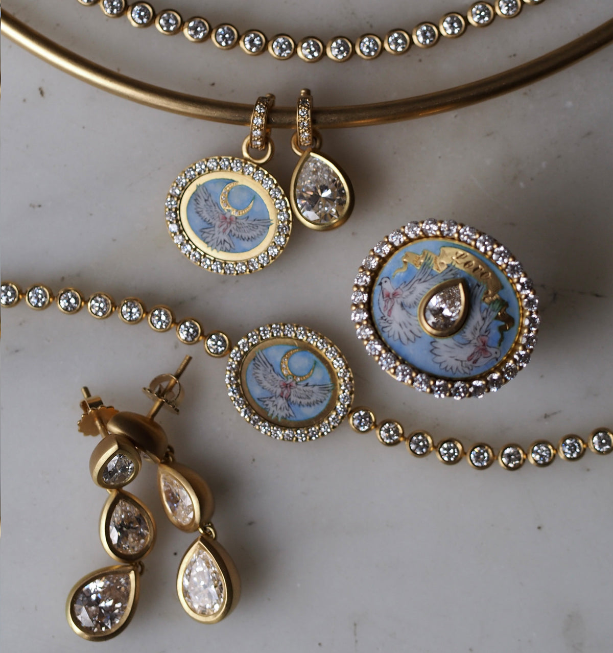 Gold pendant and earrings with enamel designs and multiple clear diamonds on a marble surface.