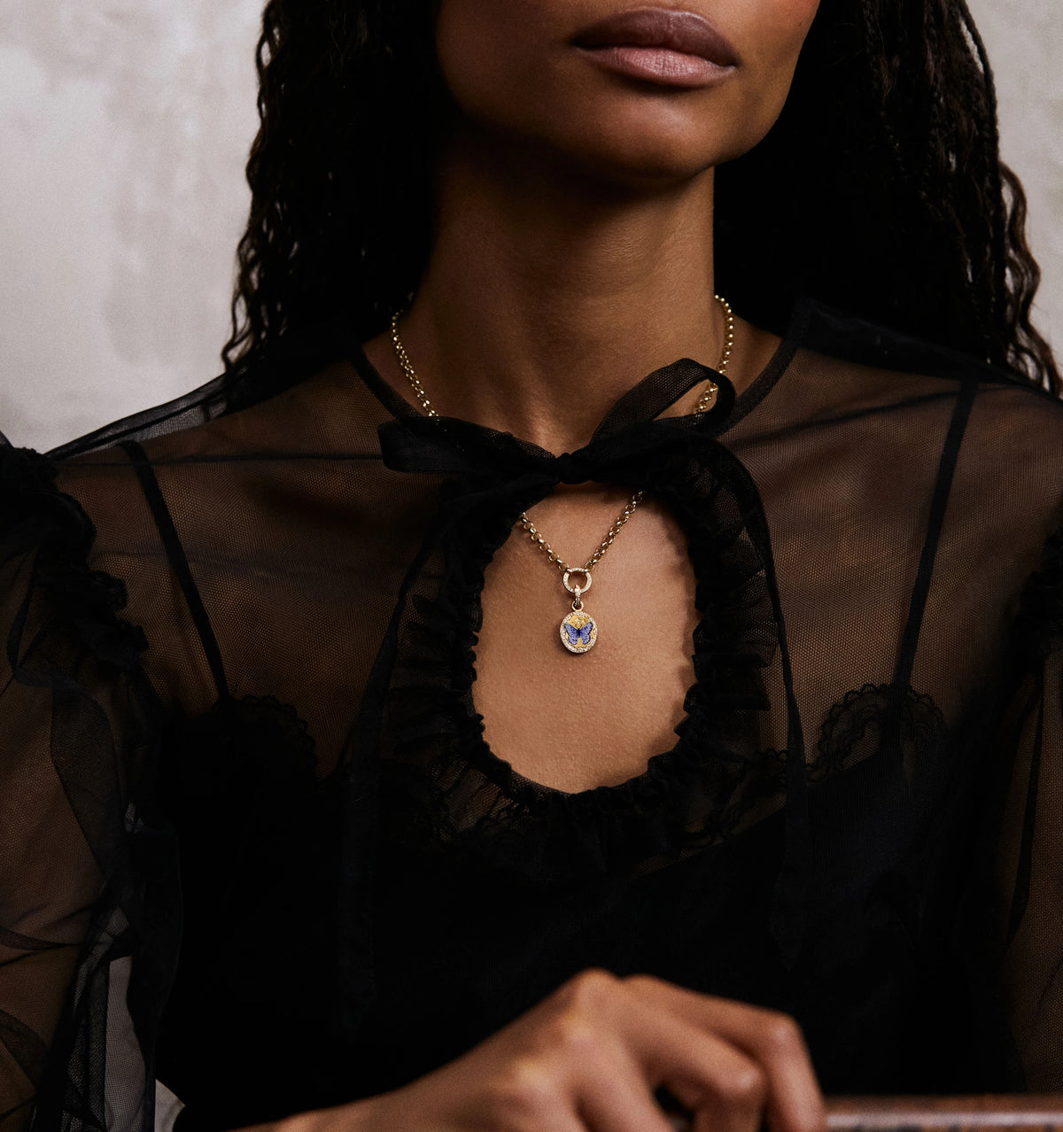 Woman wearing a gold necklace with a blue and yellow pendant, featuring a butterfly design, sitting at a table.