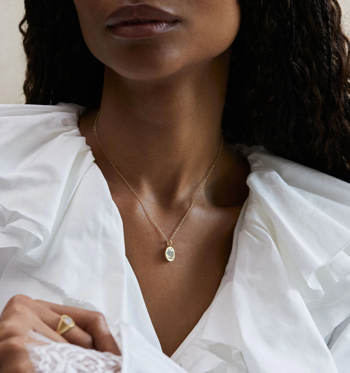 Woman wearing a gold pendant necklace with an oval design and a gold ring on her finger.