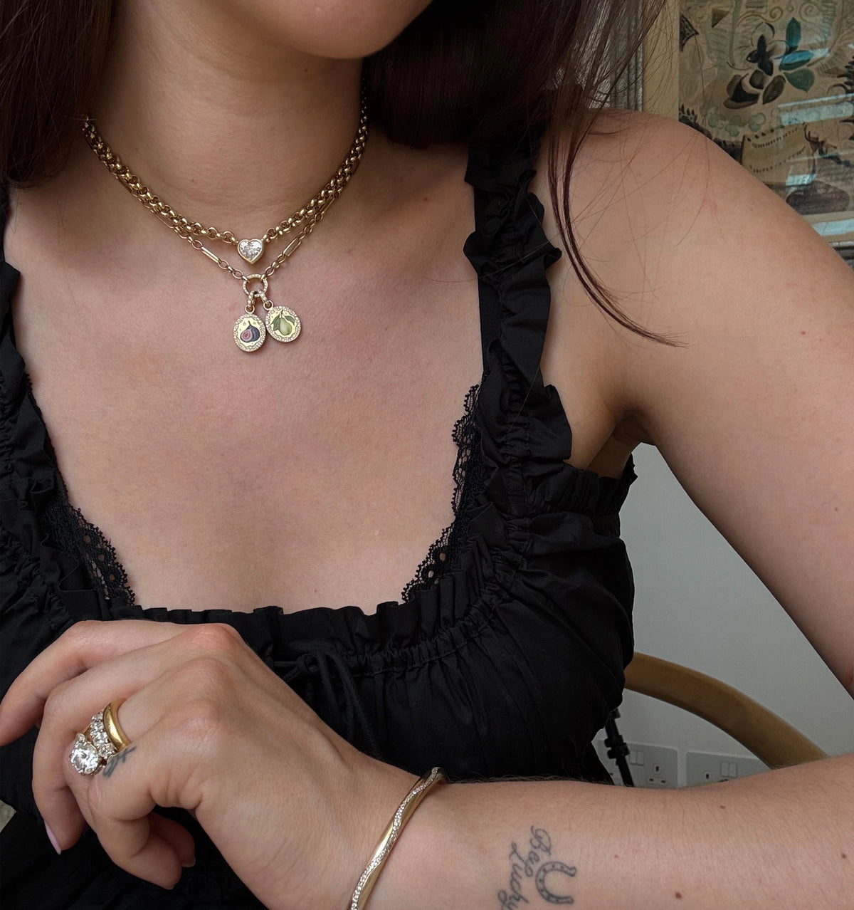 Woman wearing a gold layered necklace with heart and charm pendants and a gold ring on her hand.