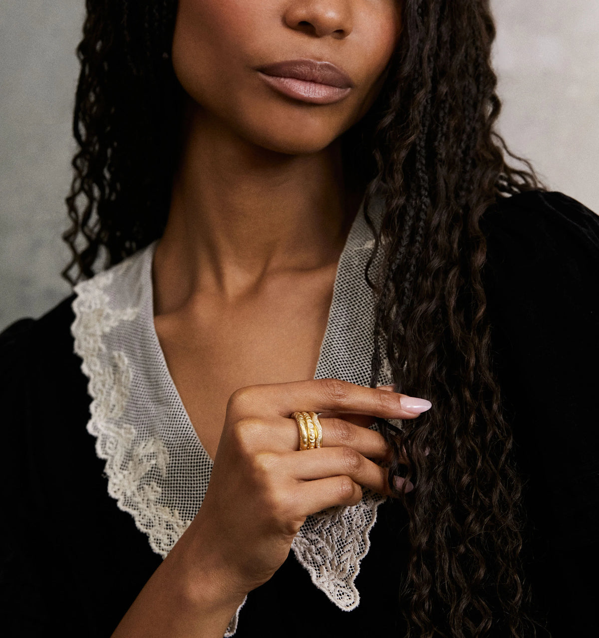 Woman wearing a gold ring, with a textured design, and styled hair against a soft neutral background.