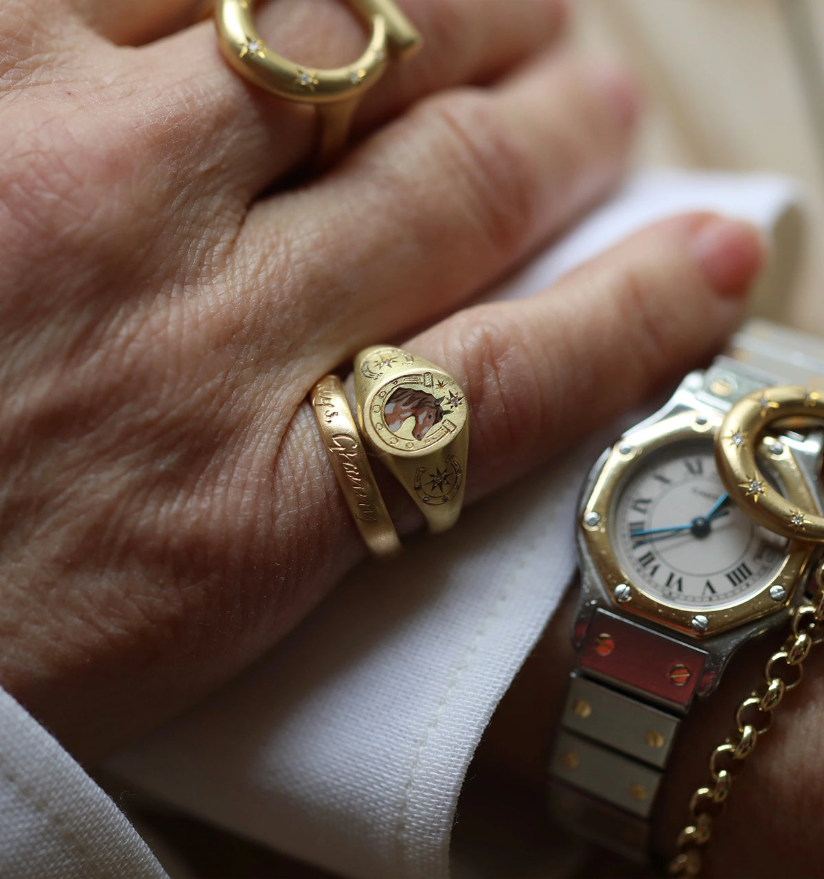 Woman wearing gold rings and a gold watch, featuring etched details and a central design.