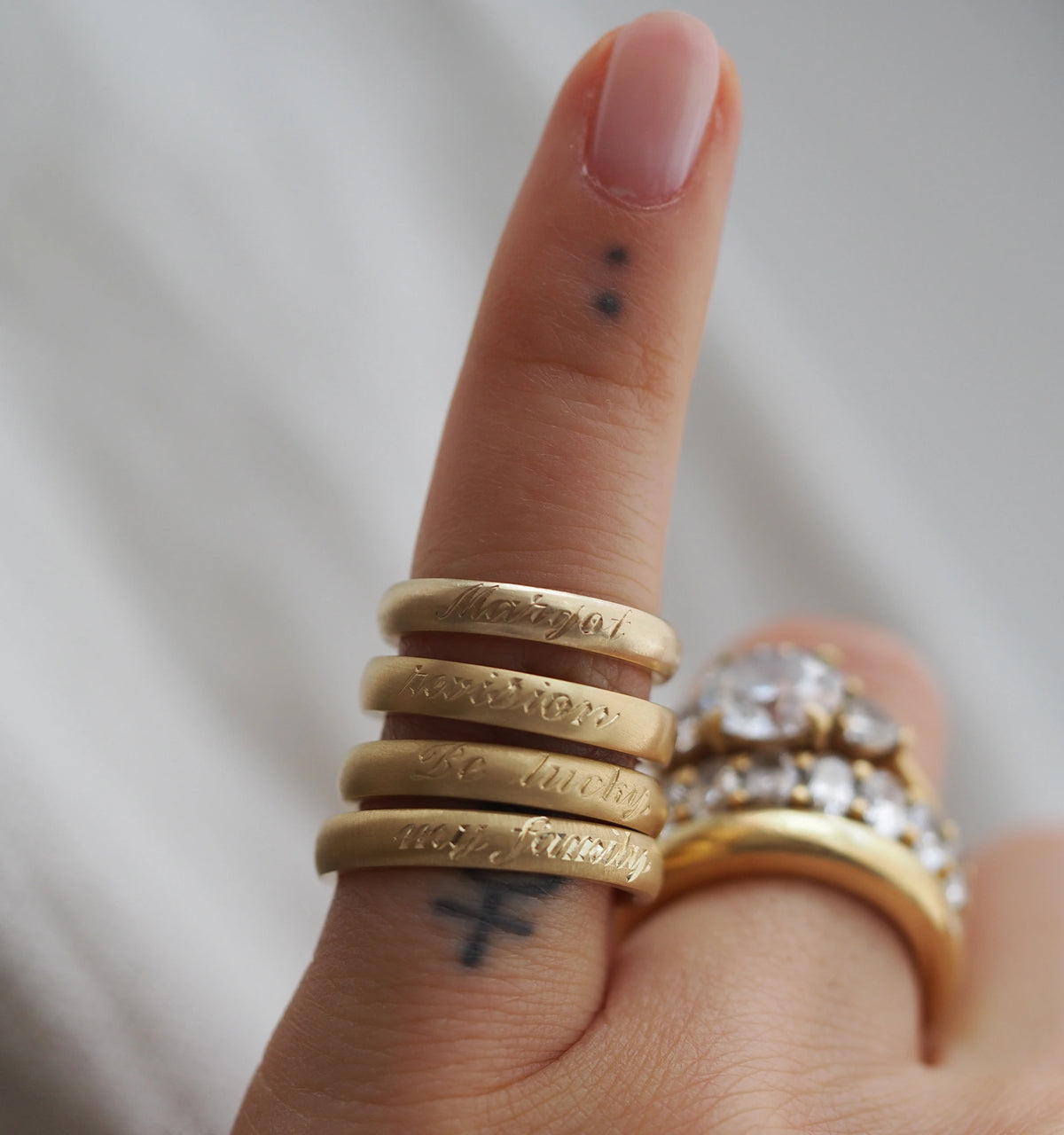 Woman wearing four gold engraved rings stacked on her finger, with a gold ring featuring a large clear stone.