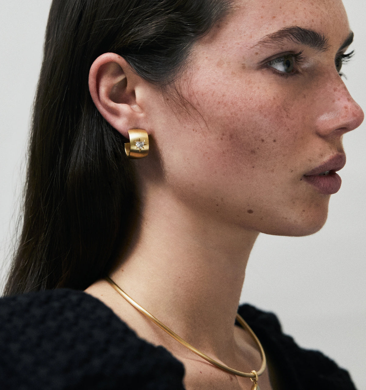 Woman wearing a gold hoop earring featuring a diamond and a gold collar necklace.