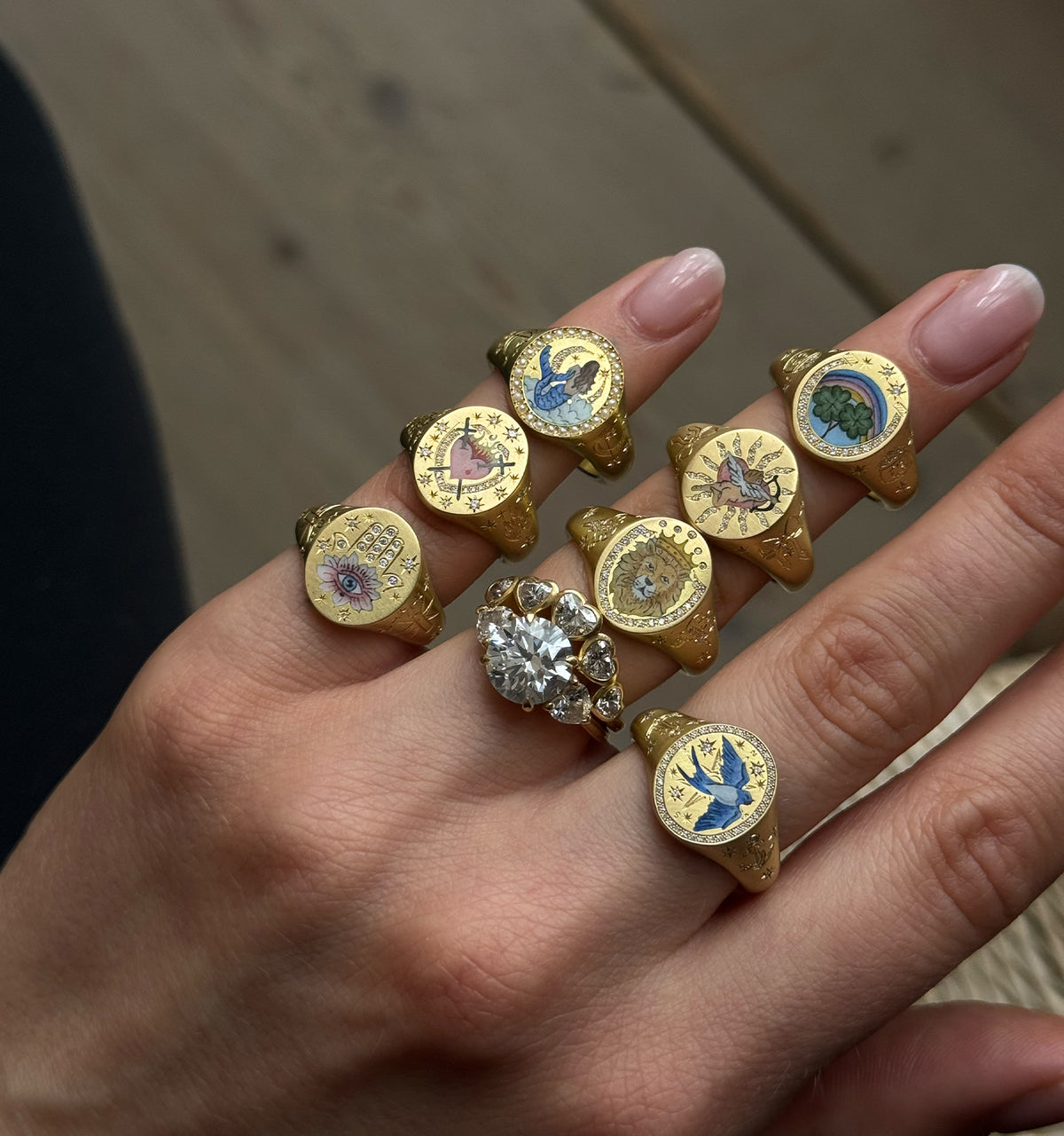 Woman wearing multiple gold rings with colourful decorative motifs and a central gold ring adorned with a large stone.