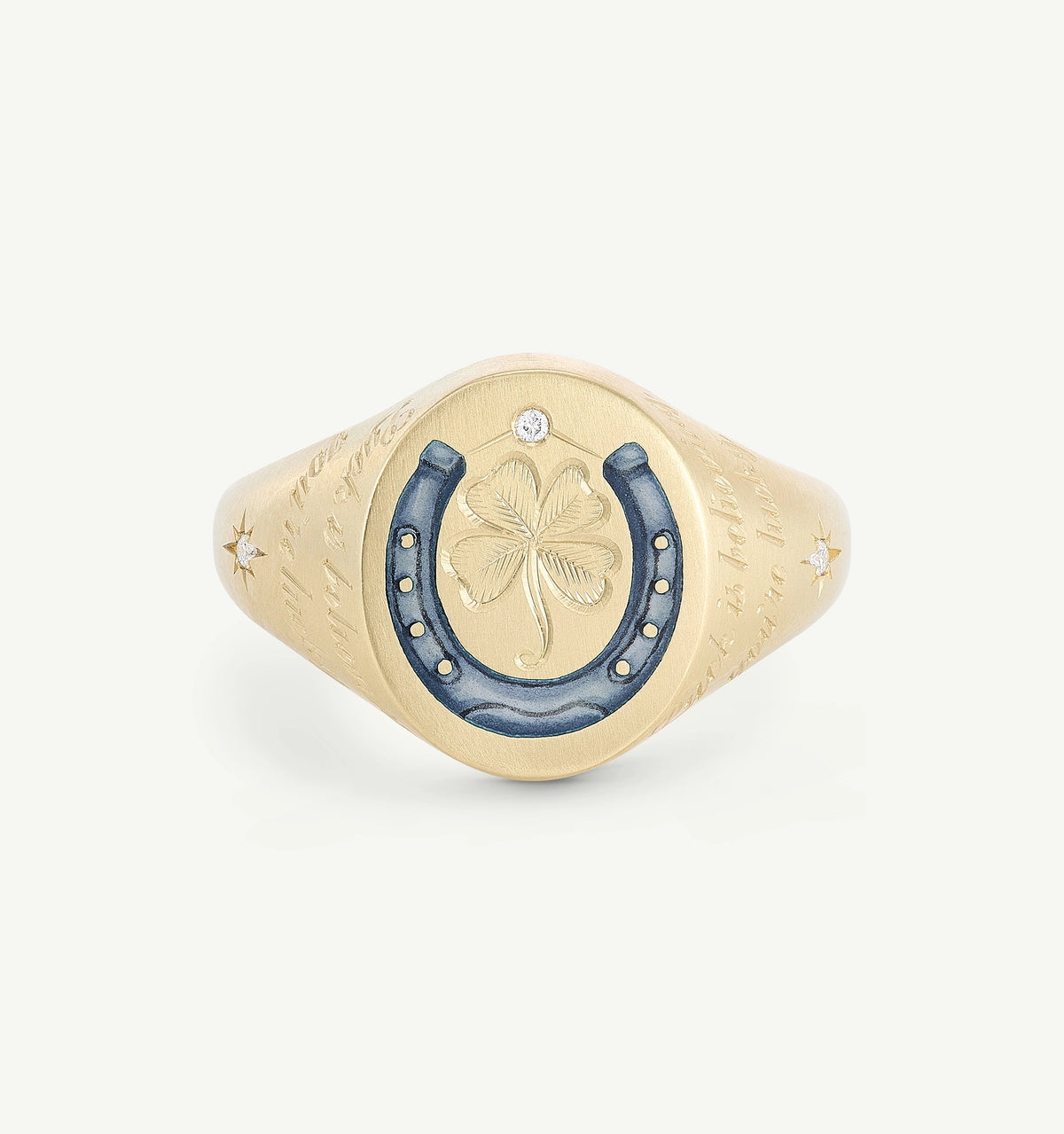 Gold signet ring featuring a blue enamel horseshoe, clover engraving, and two diamonds on a smooth surface.
