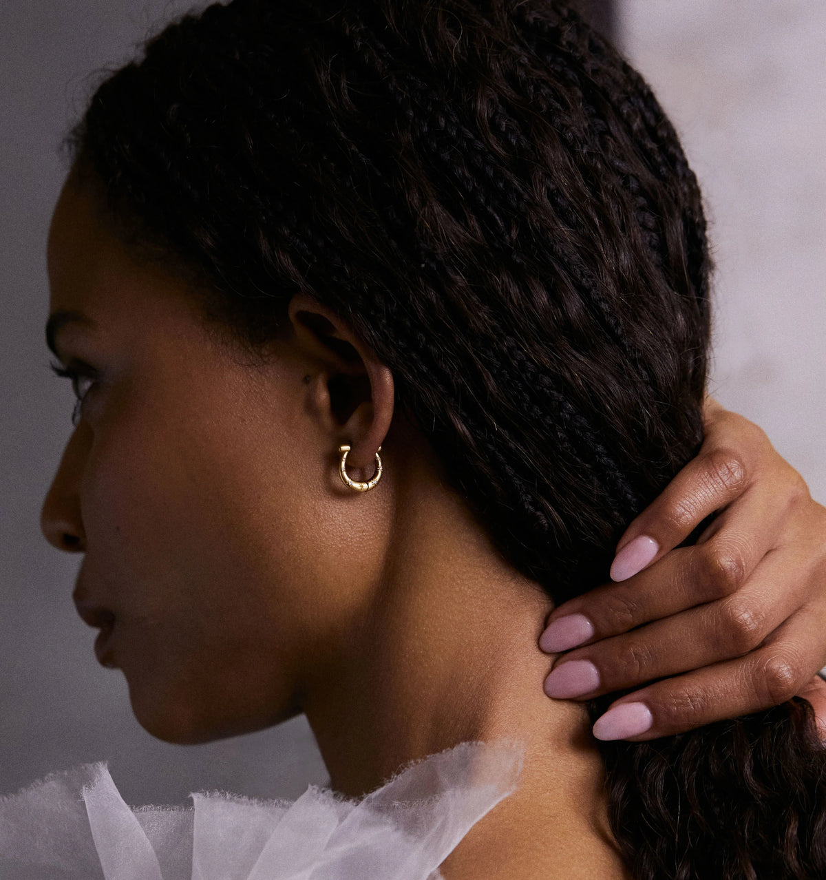 Woman wearing a gold hoop earring, with her hand gently resting on her neck.