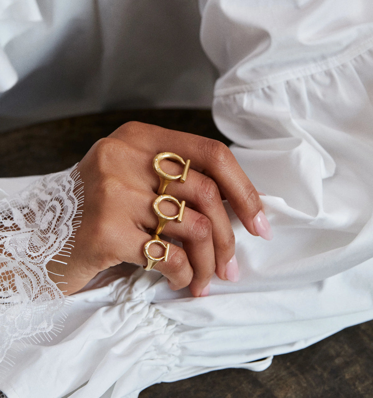 Woman wearing three gold rings featuring a horseshoe design, resting on a white fabric surface.