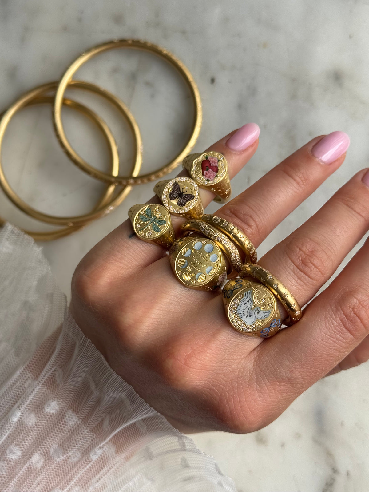 Woman wearing multiple gold rings with various motifs, including butterflies and hearts, alongside gold bangles.