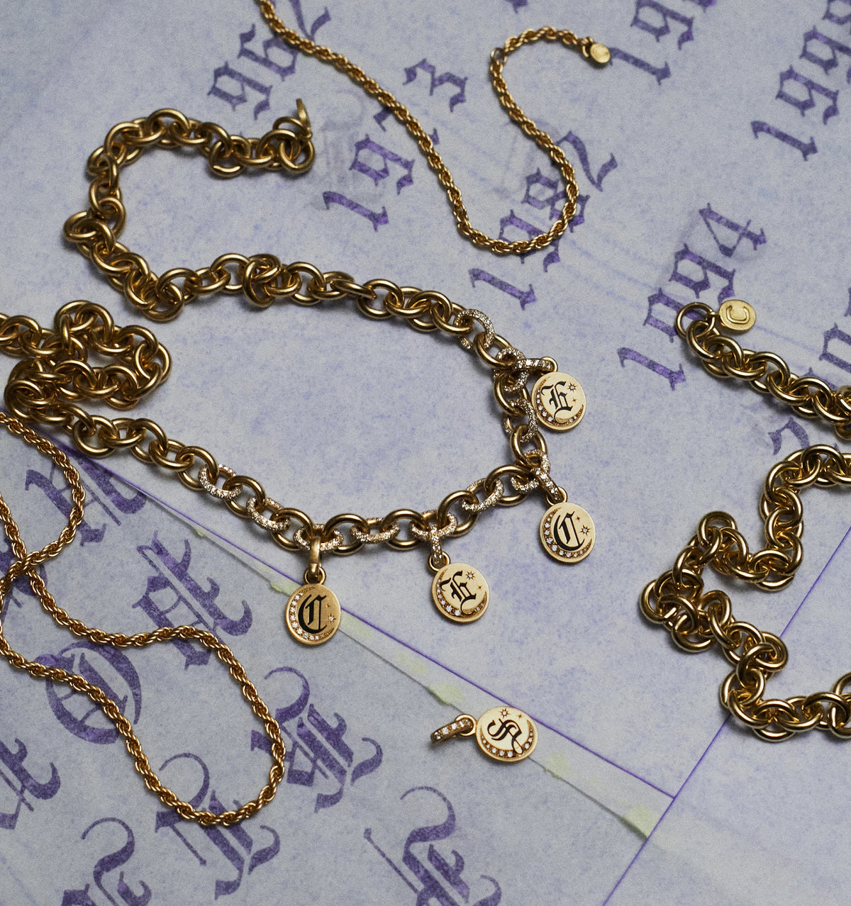 Gold bracelet with engraved charms, displayed on vintage-inspired paper with purple text and accents.