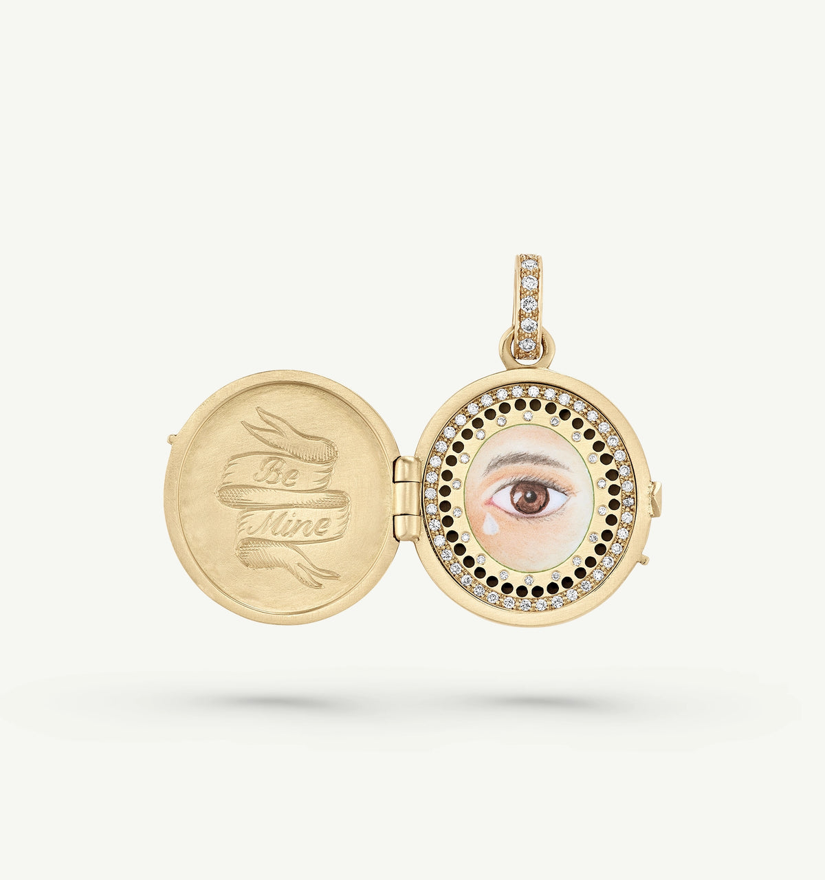 Gold locket pendant featuring a painted eye and the engraving "Be Mine," surrounded by a circle of diamonds.