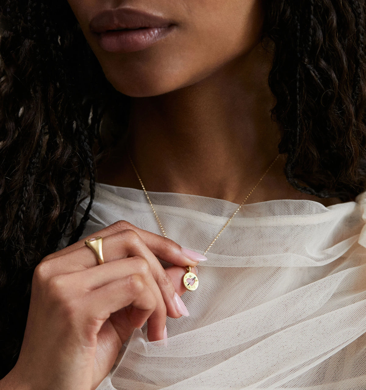 Woman wearing a gold necklace with a pendant and a gold ring, styled with a soft, sheer fabric.