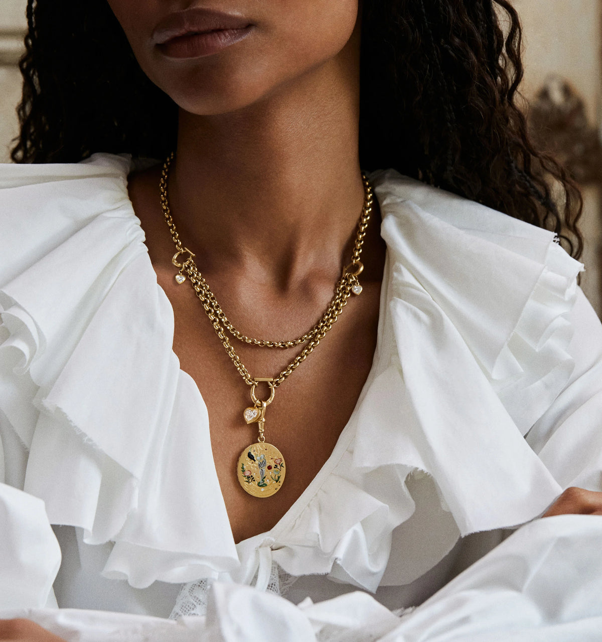 Woman wearing layered gold chain necklaces featuring a decorative pendant with floral motifs.