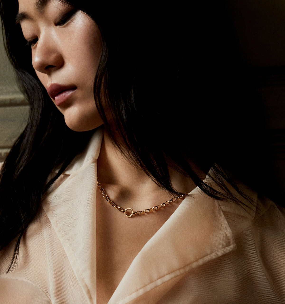 Woman wearing a gold chain necklace with a circular pendant, paired with a light-coloured blouse.