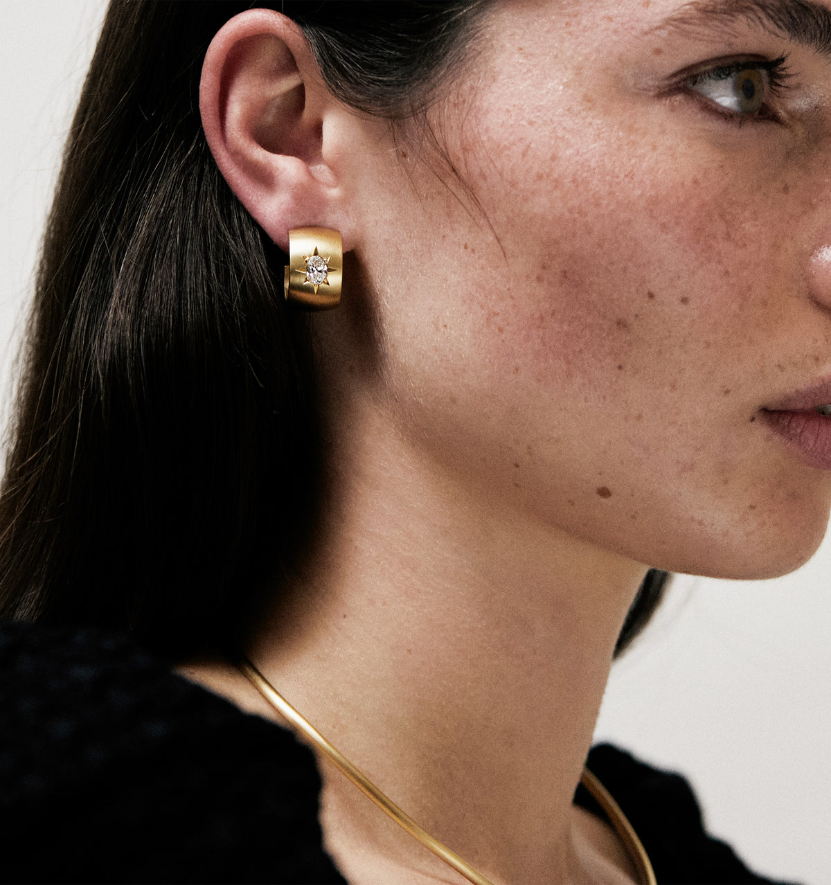 Woman wearing a gold hoop earring featuring a star design and a gold necklace.
