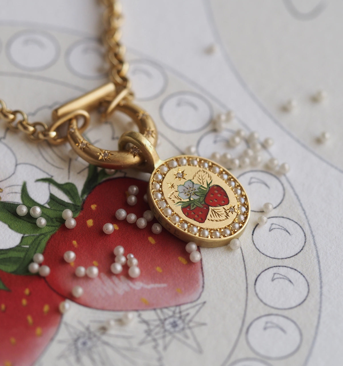 Gold pendant featuring a strawberry illustration with an enamel finish, surrounded by decorative pearls on a floral background.