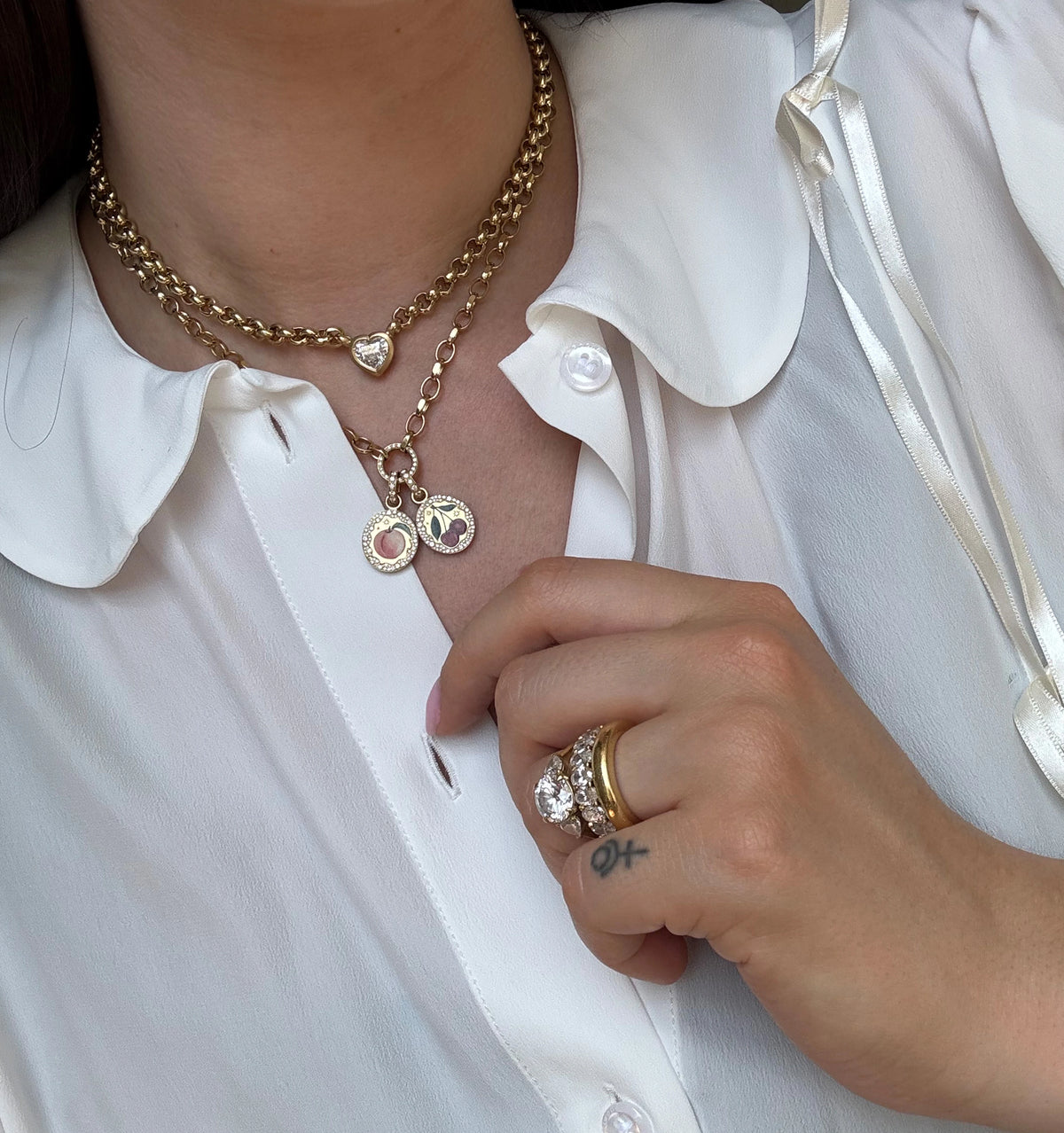 Woman wearing layered gold necklaces with heart charms and gold rings on her hand.