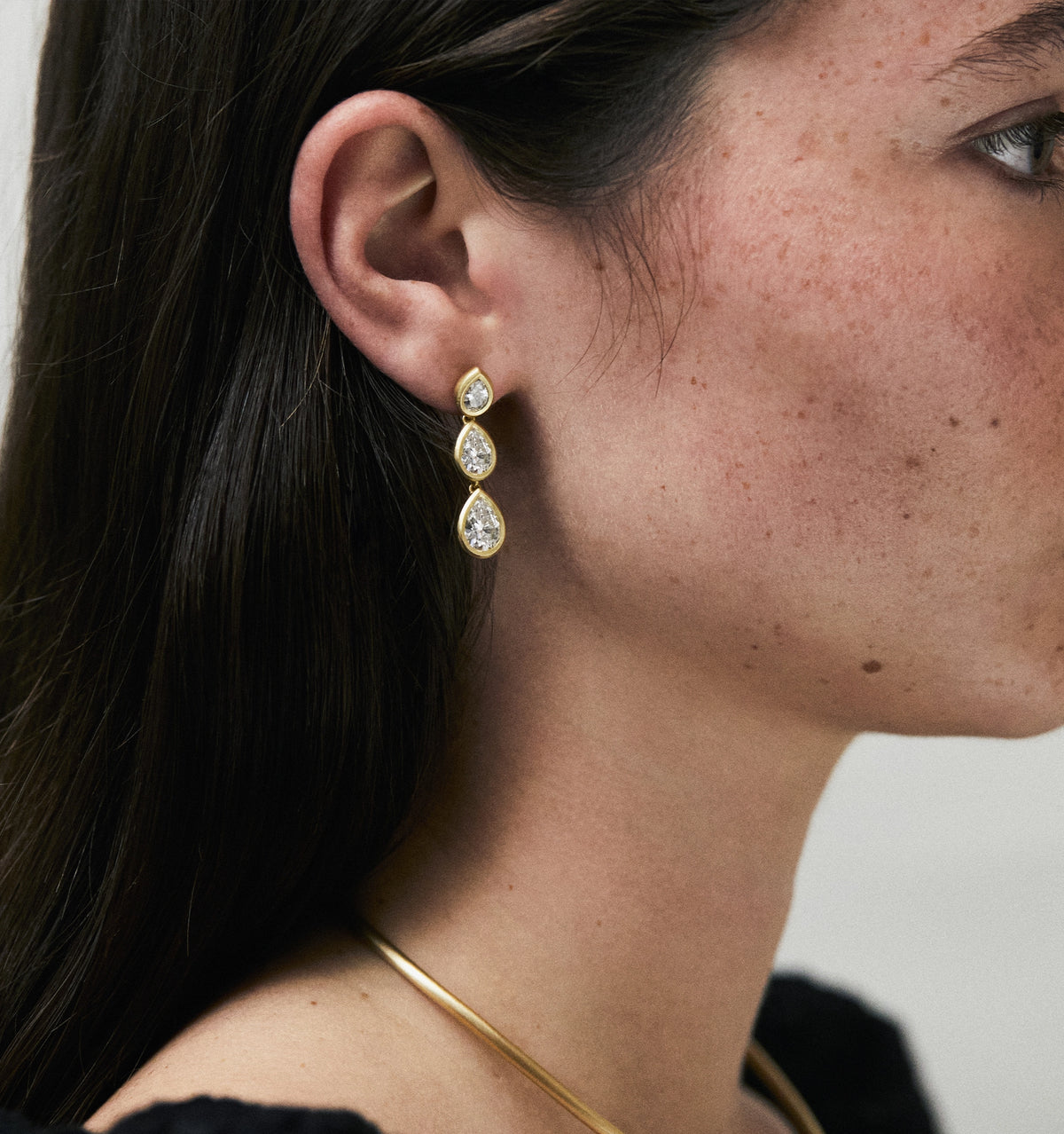 Woman wearing gold earrings with three teardrop-shaped diamonds.