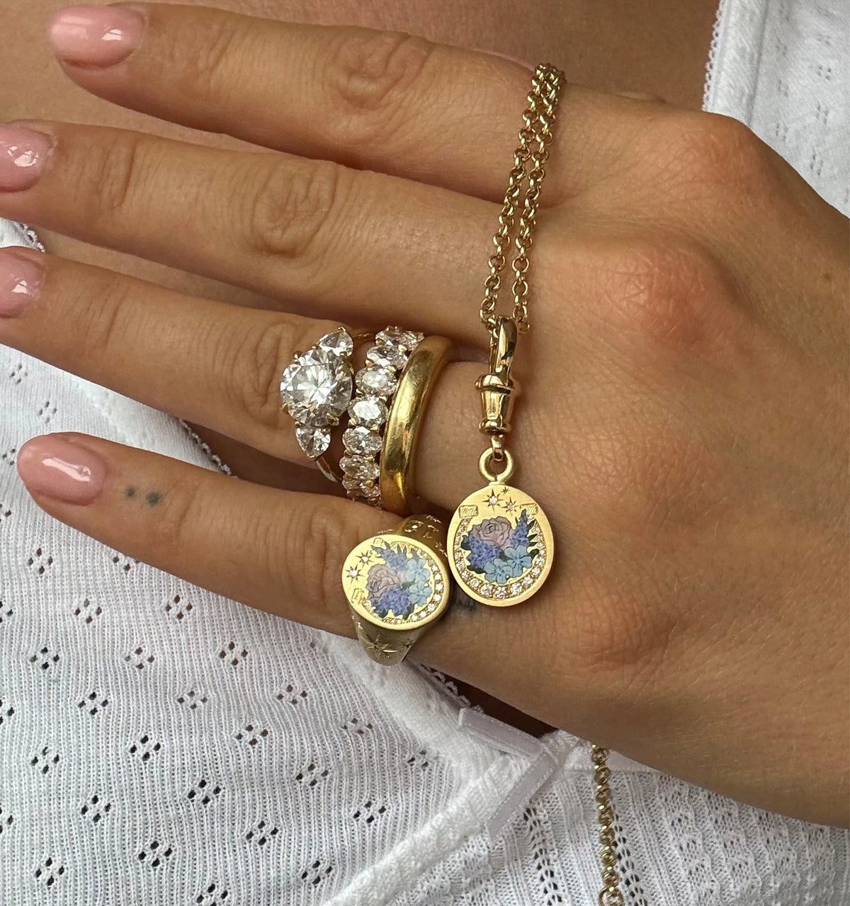Woman wearing gold rings and a pendant featuring floral designs with coloured enamel and diamonds.