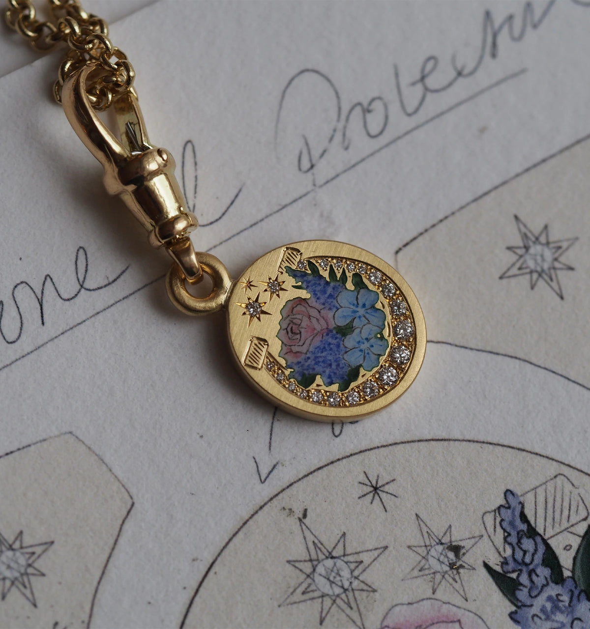 Gold pendant featuring an engraved floral design and surrounded by diamond accents on a textured background.
