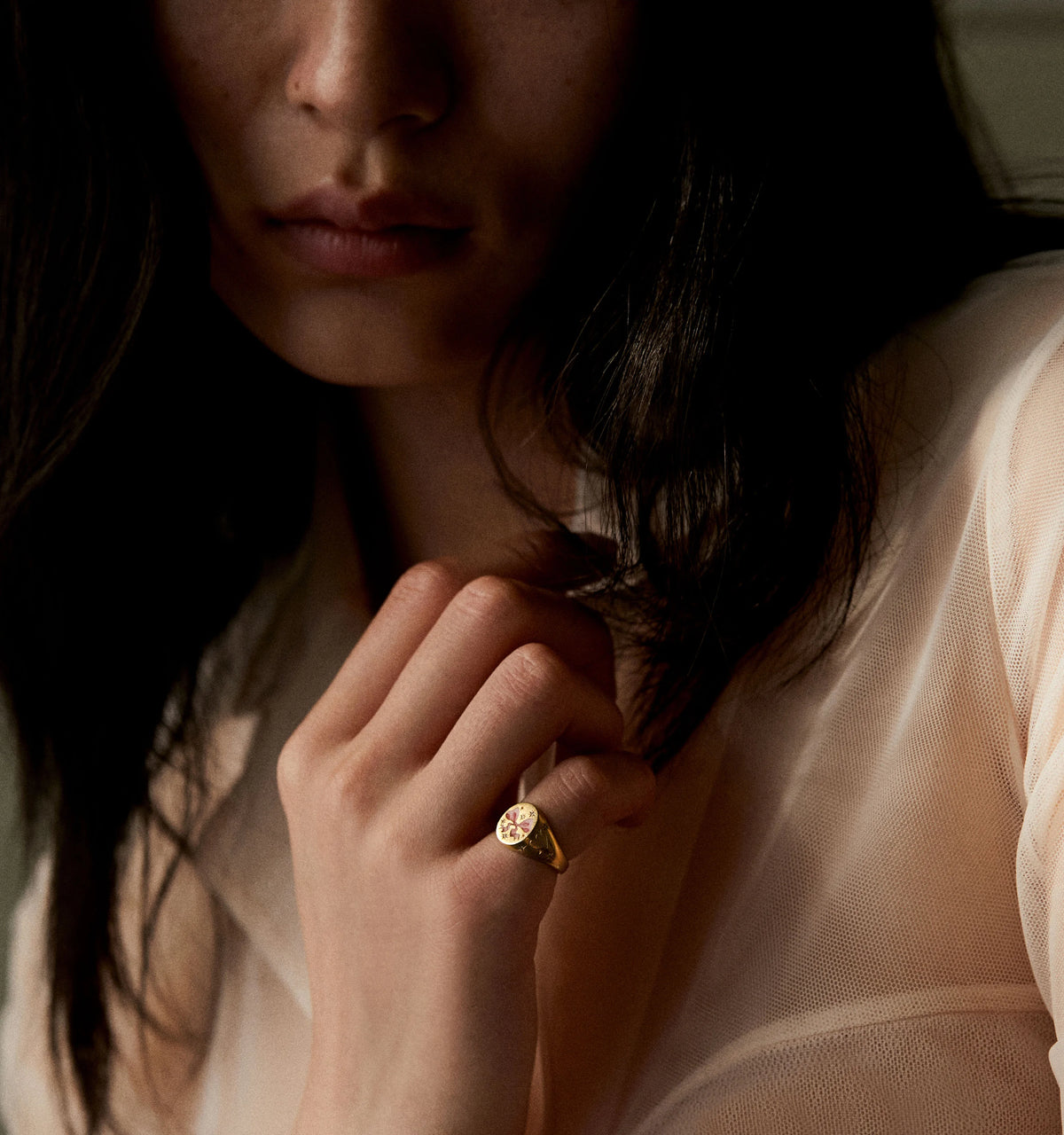 Woman wearing a gold ring with a round pink stone, holding her hand near her face in soft lighting.