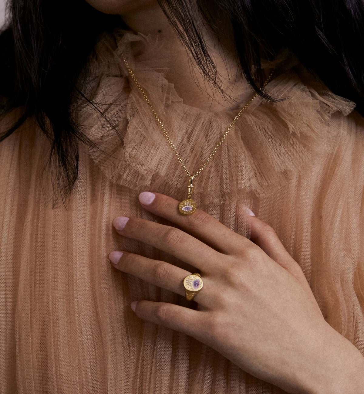 Woman wearing a gold necklace with a pendant and a gold ring.
