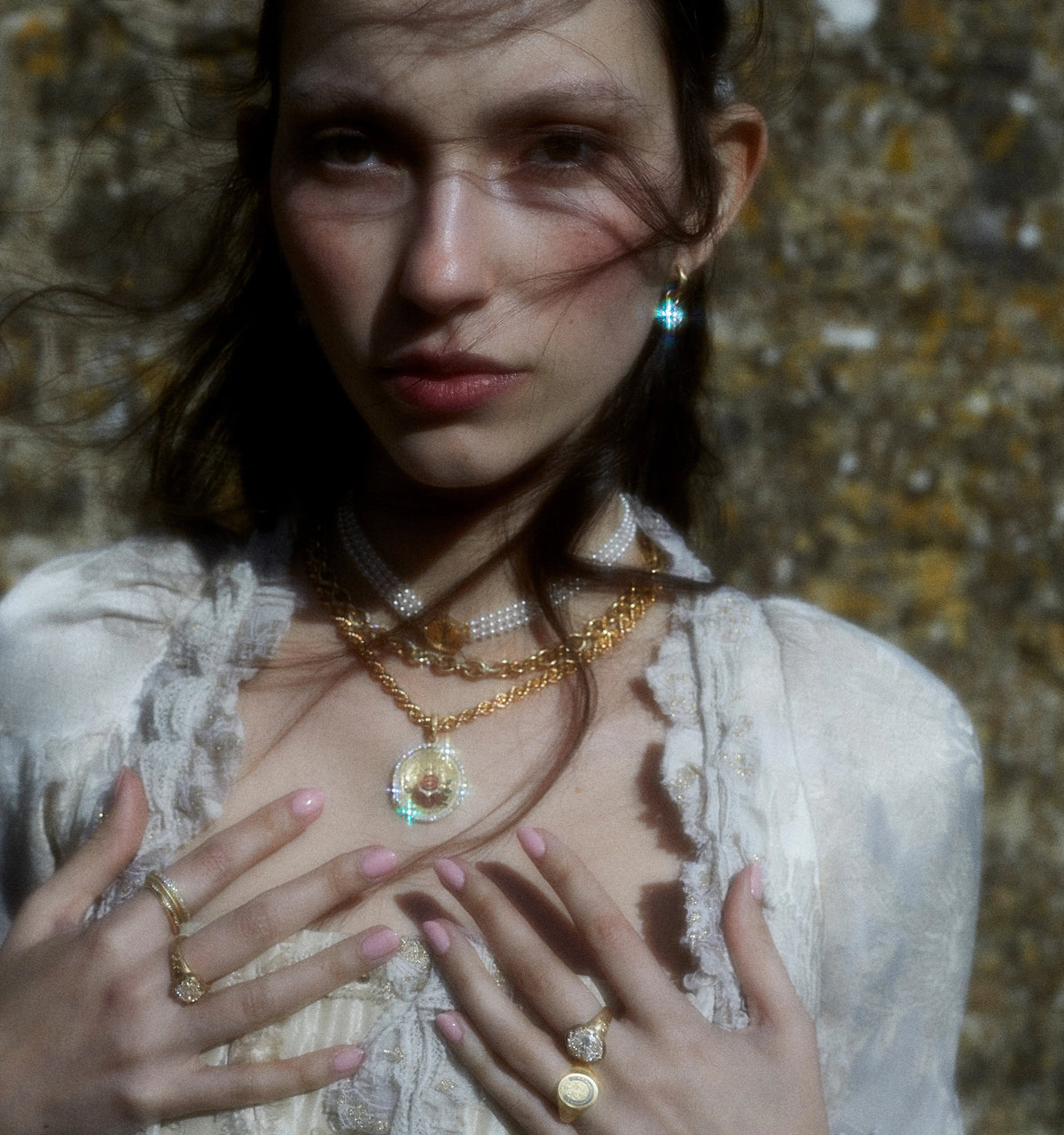 Woman wearing layered gold necklaces with a diamond pendant, a diamond drop earring, and multiple diamond rings on her hands.