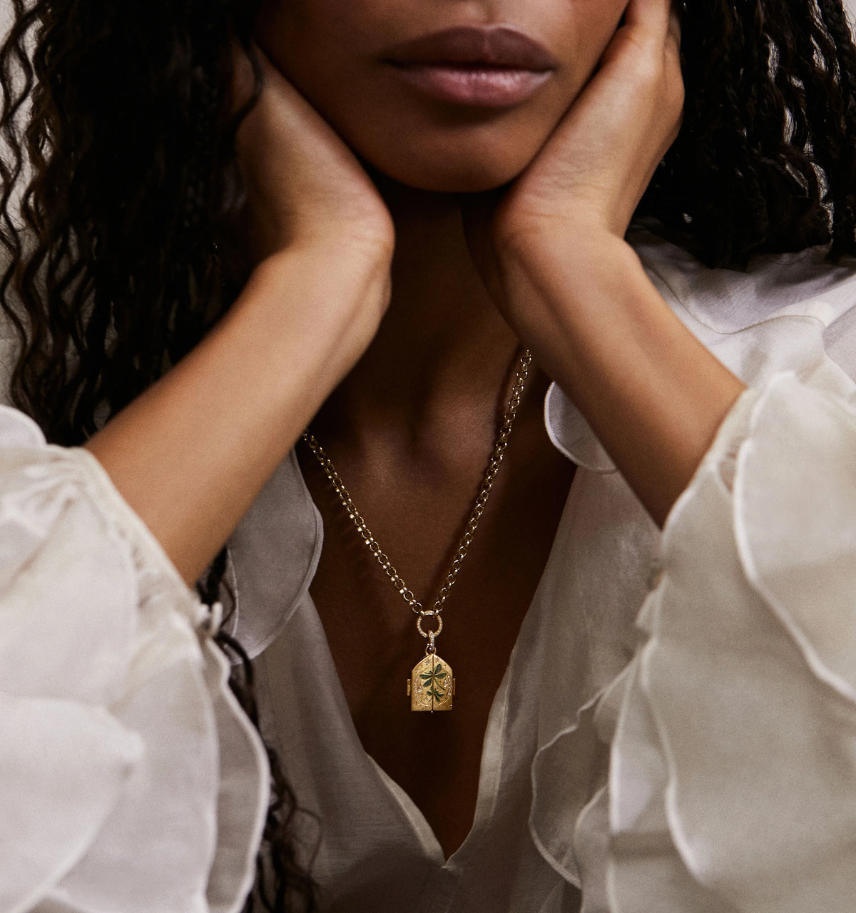 Woman wearing a gold pendant necklace featuring an engraved design, styled with a white blouse.