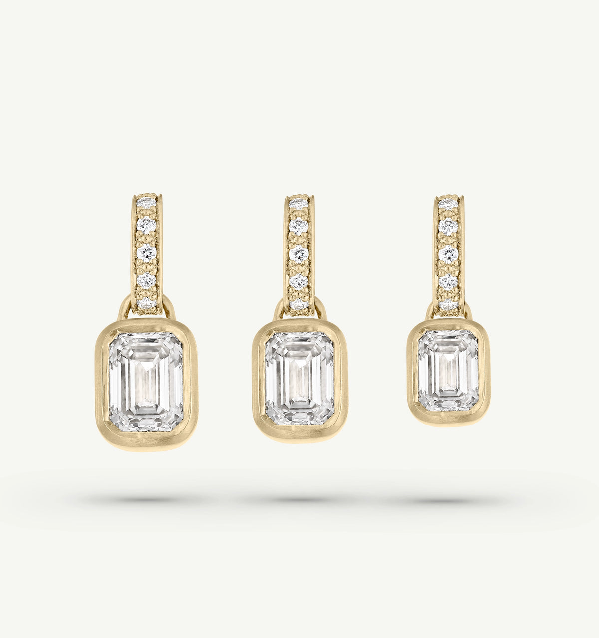Gold earrings featuring emerald-cut diamonds with a pavé setting above each stone.