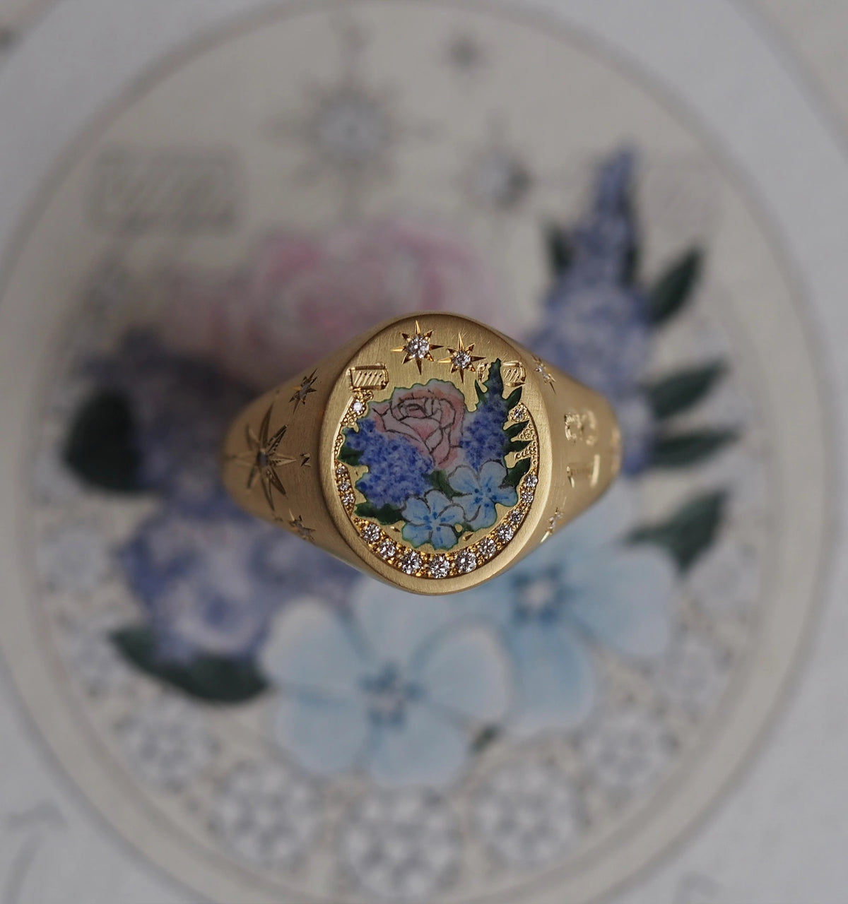 Gold ring featuring a floral enamel design with pink roses and blue flowers, surrounded by gold star engravings.