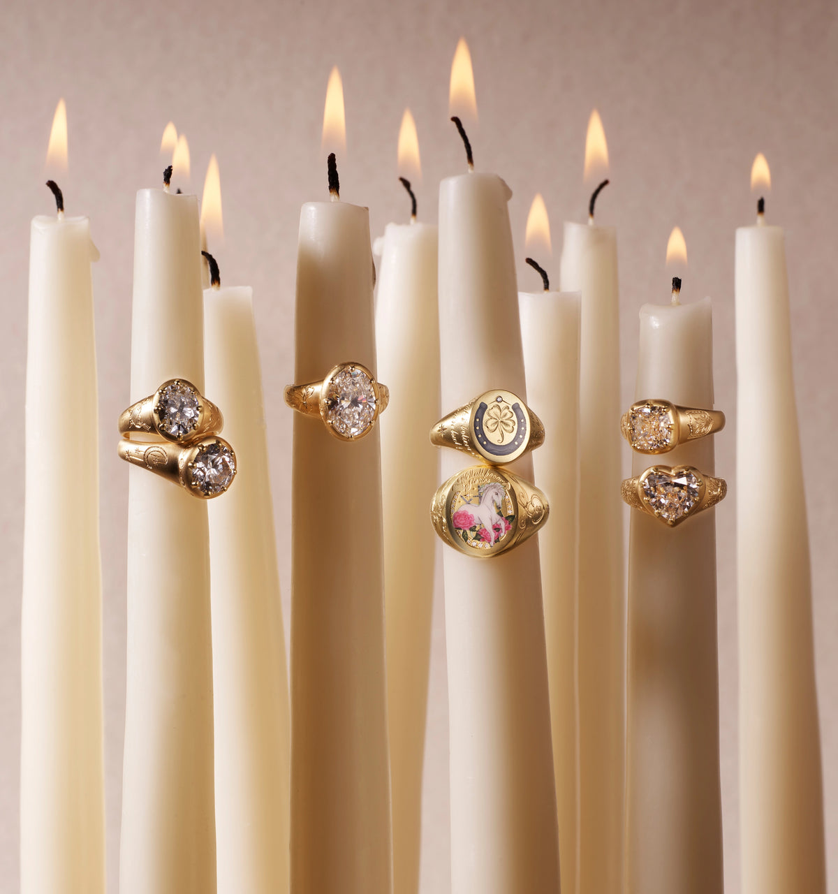 Gold rings with various designs, including one featuring a unicorn, displayed among white candles.