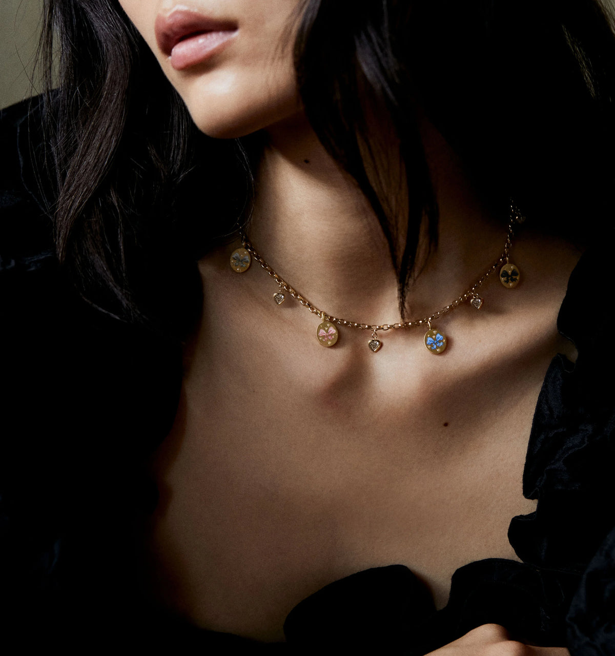 Woman wearing a gold necklace with colourful enamel pendants and heart charms.