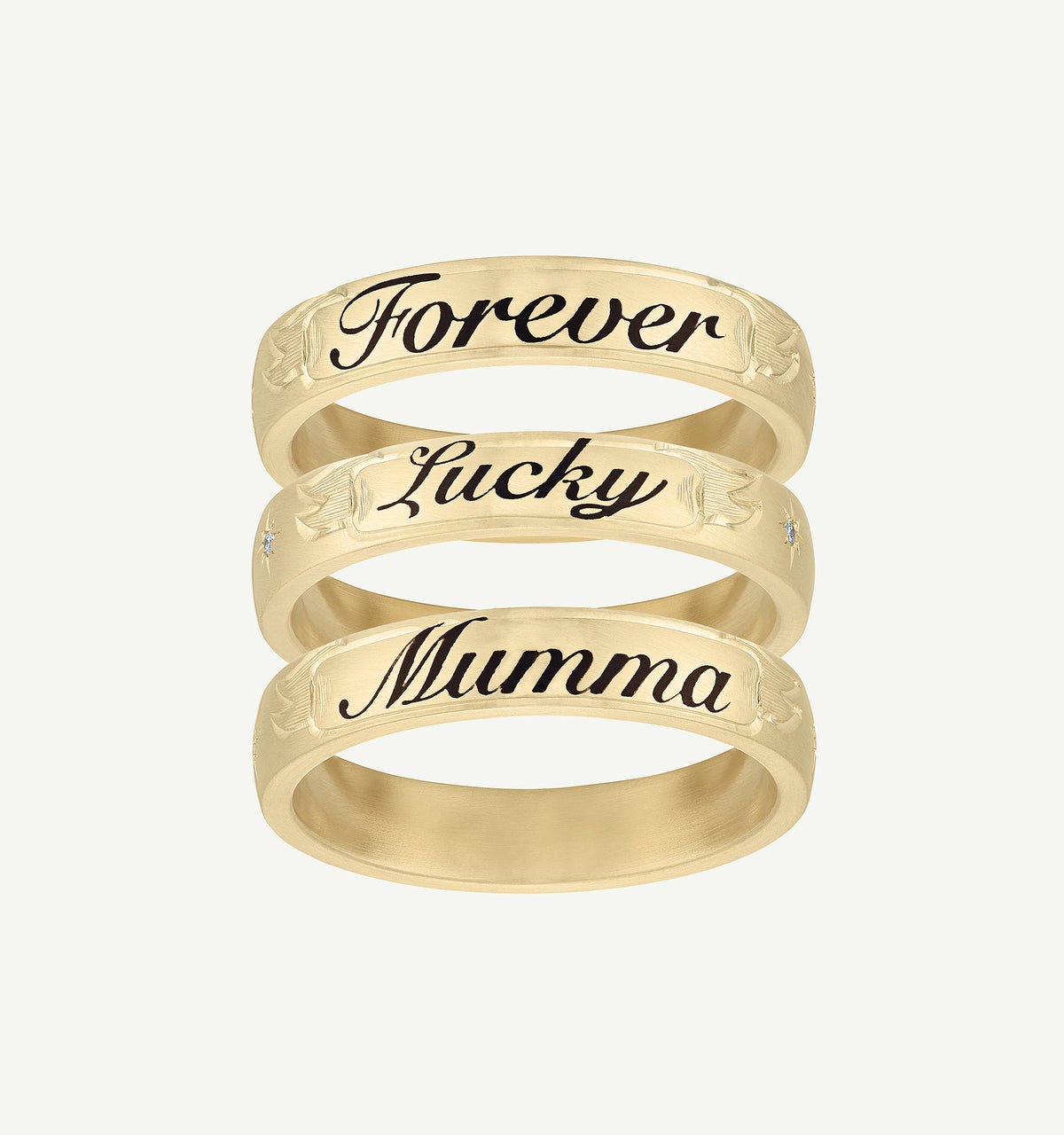 Gold stackable rings with engraved words "Forever," "Lucky," and "Mumma," featuring a small diamond accent.